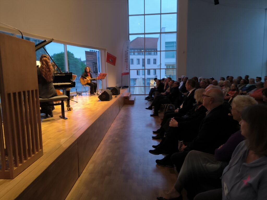 Auf dem Bild ist Turiner Trio „La Desbandá“ bei seinem Auftritt zum 80. Jahrestag der Befreiung vom Faschismus im Stadthaus Ulm und die ersten Reihen des Publikums. Von dem Trio sind Tiziana Cappellino am Flügel und die Gitarristin und Sängerin Angeles Agyado zu sehen. Foto: Johannes Glembek